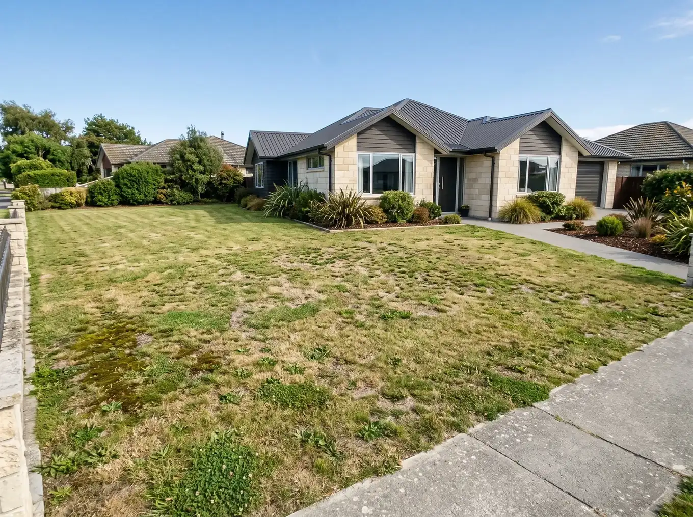 Thin, weedy and mossy front lawn with yellowish patches in front of a modern home in Oamaru